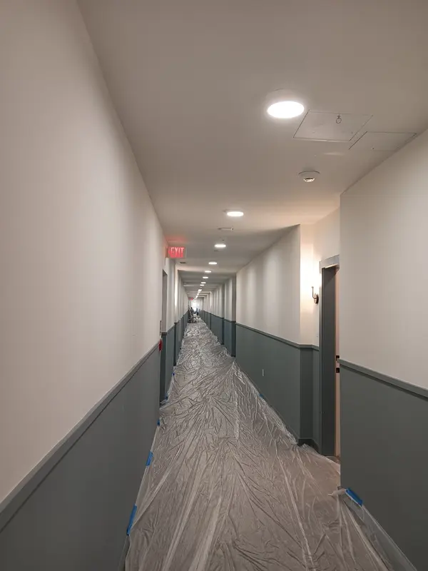 Long apartment corridor with gray wainscot paint, white upper walls and plastic floor protection