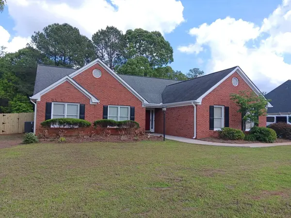 Red brick ranch home with black shutters and white trim behind a wide front lawn