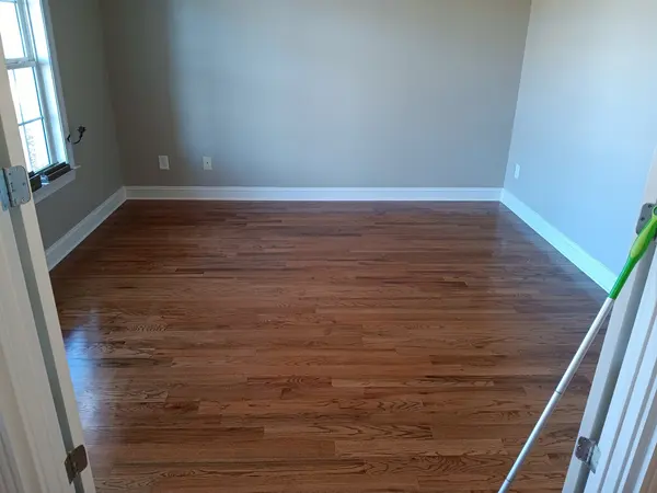 Freshly refinished red oak floor in an empty room with gray walls and white baseboards