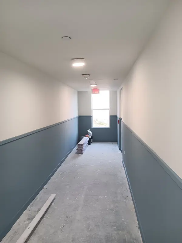Corridor with dark gray lower walls and white upper walls over a bare concrete floor