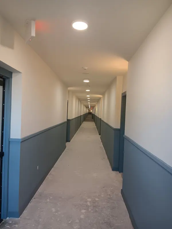 Long corridor with blue-gray wainscot paint and white walls, concrete floor not yet covered
