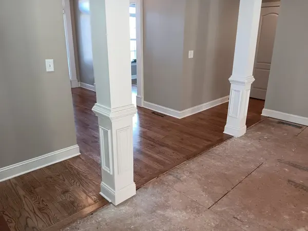 New hardwood flooring laid around white square columns, bare subfloor still showing in the next room