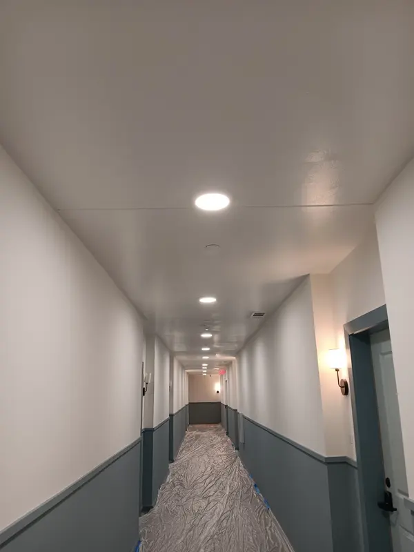 Corridor with gray wainscot, white walls and wall sconces, floor still under protection