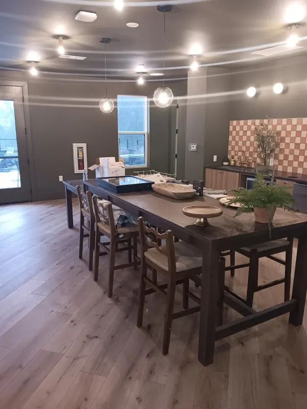 Clubroom with gray walls, wood-look plank floor and a long dining table under pendant lights