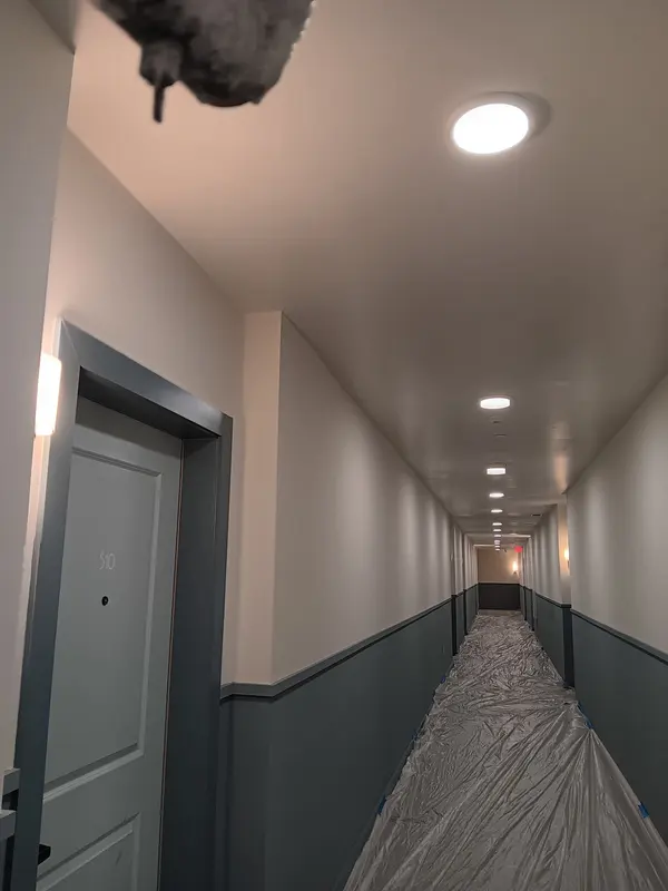 Corridor with a gray unit door, two-tone walls and plastic sheeting over the floor