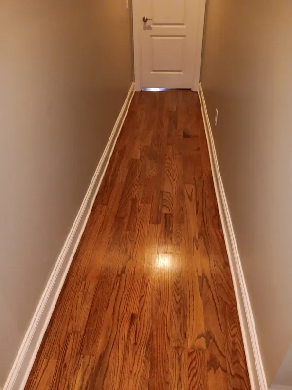 Narrow hallway with glossy refinished oak flooring and white baseboards