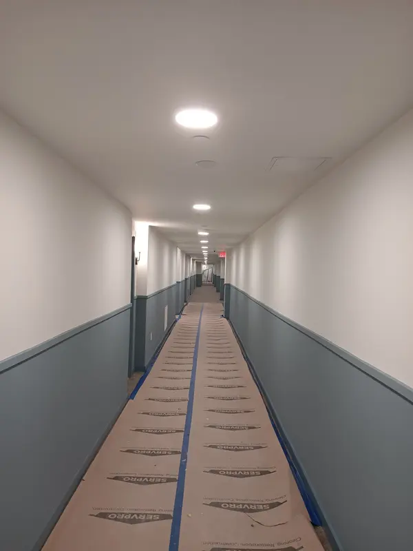 Long corridor with gray lower walls and white upper walls, paper protection taped along the floor