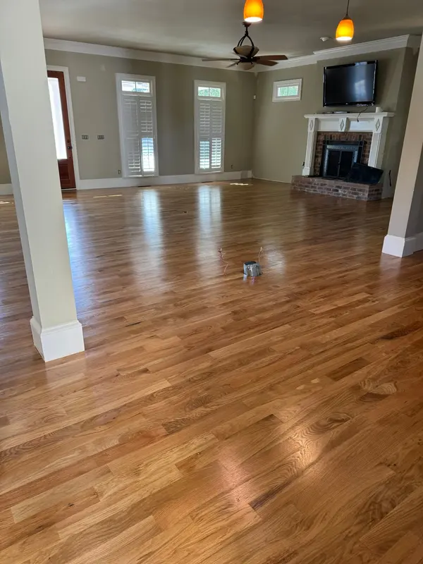 Open living room with glossy refinished oak floors, a brick fireplace and white columns