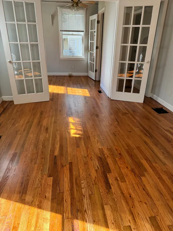 Sunlit room with refinished red oak floors framed by open French doors