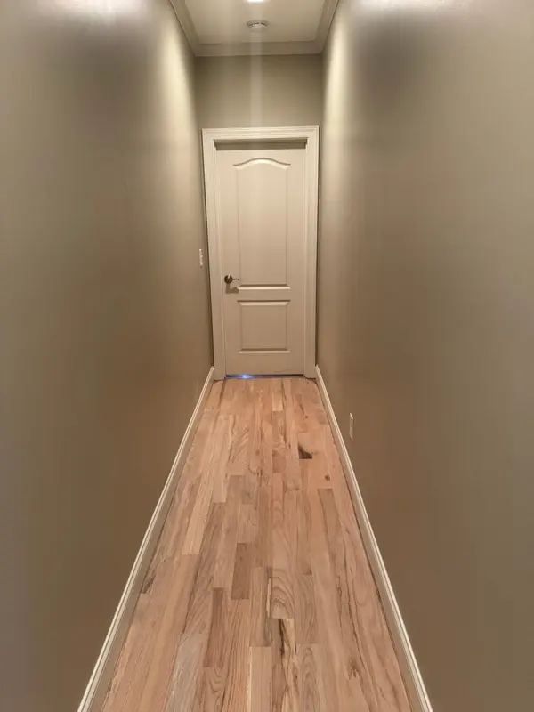 Narrow hallway with new unfinished oak flooring leading to a white door