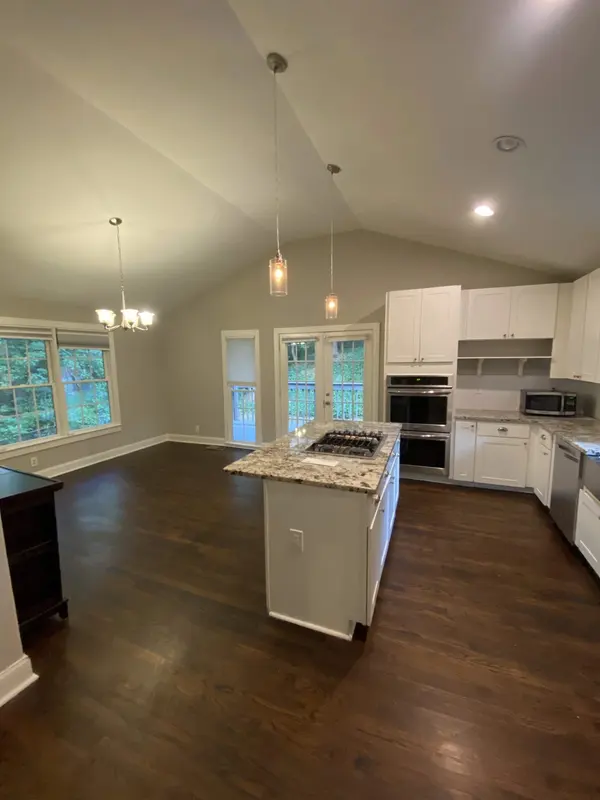 Vaulted kitchen with white cabinets, a granite island and dark wood floors
