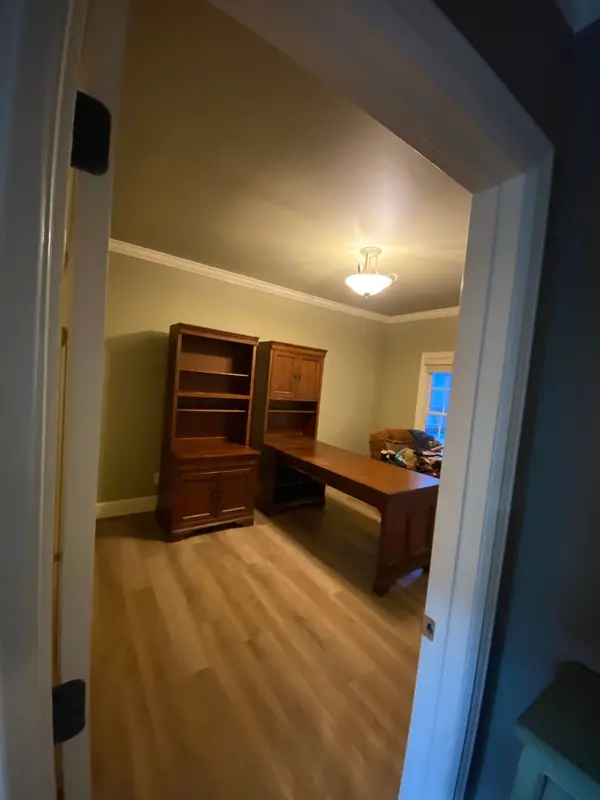 Home office painted olive green, with a wood desk and hutch on light flooring