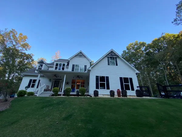 White two-story farmhouse with black shutters and a covered front porch under a clear sky