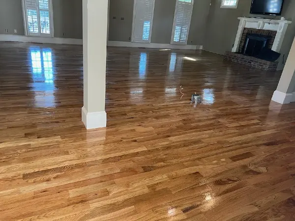 Glossy wet-finish oak floor in a large living room with a white column and brick fireplace