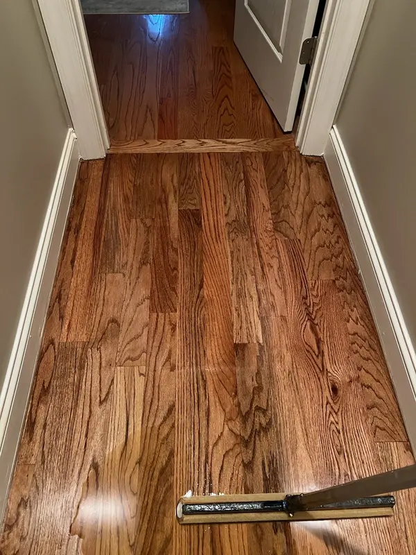 Refinished red oak floor through a narrow hall with a floor vent cover set aside
