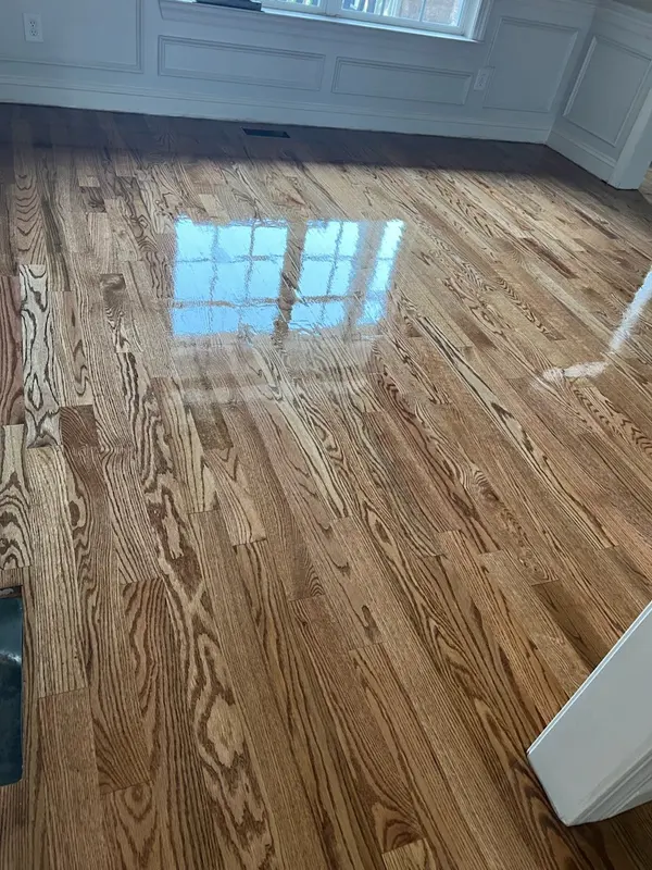Glossy refinished oak floor reflecting a window in a room with white wainscoting
