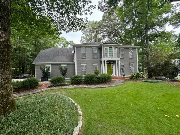 Gray painted colonial with white columns, a yellow front door and a landscaped lawn