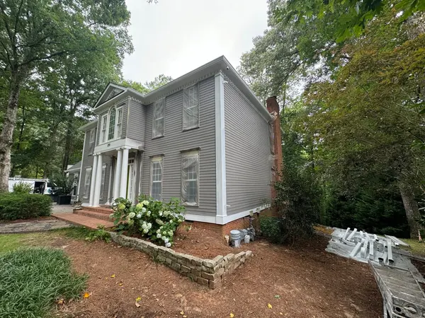 Side of a gray colonial with white corner boards, ladders and materials staged on the mulch