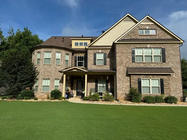 Large brick and tan siding home with a turret bay and covered porch behind a green lawn