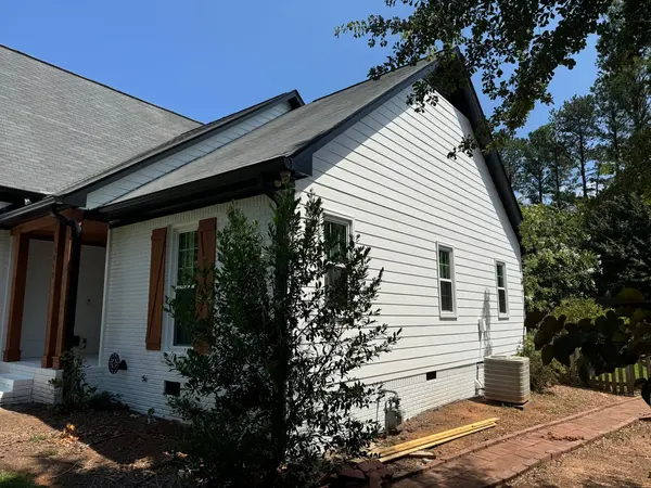 Side of a white painted lap siding home with cedar-tone shutters and a stained porch post