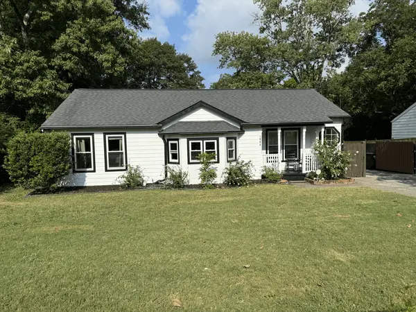 White painted cottage with black window trim and a small front porch behind a lawn