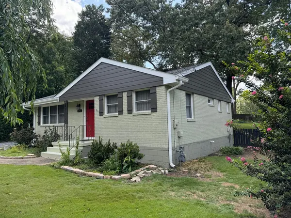 Small sage green painted brick home with dark gray gable siding and a red door