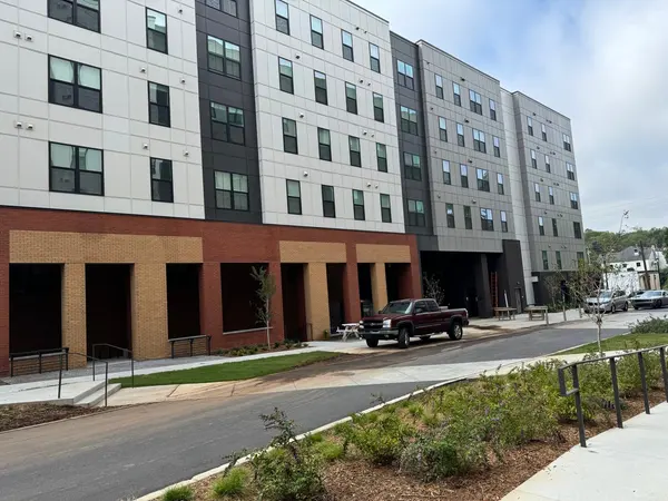 Apartment building with white, gray and charcoal panels above a brick and tan ground floor