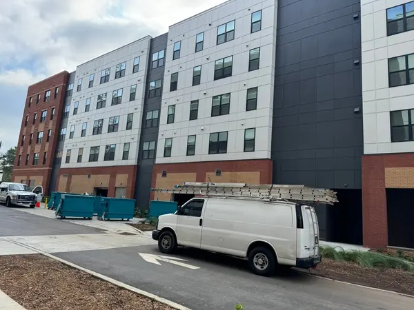 Mid-rise apartment exterior with a white work van and ladders parked along the drive