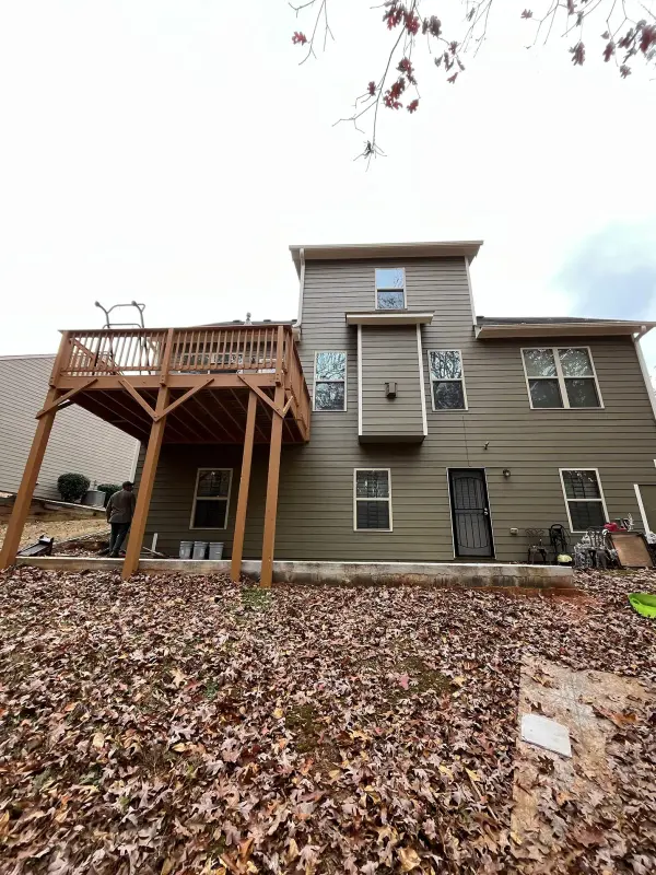 New raised pressure-treated deck on the back of a two-story home with tan siding