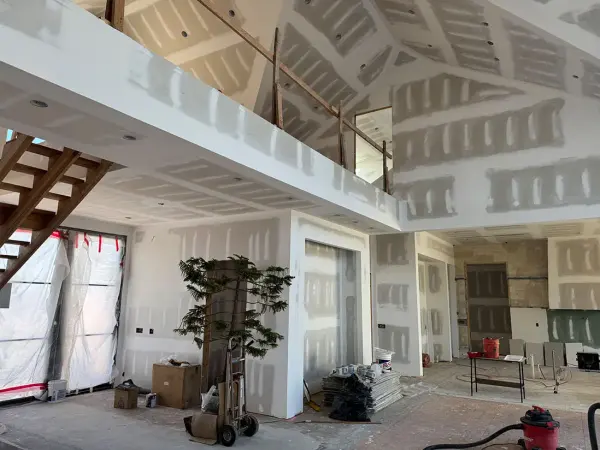 Two-story room with new drywall taped and mudded, plastic over the windows and tools on the floor