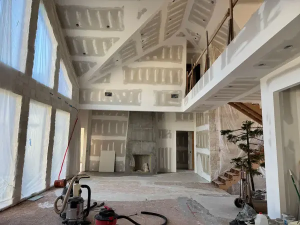 Vaulted great room with fresh drywall mud on every seam, a stripped fireplace and shop vacs