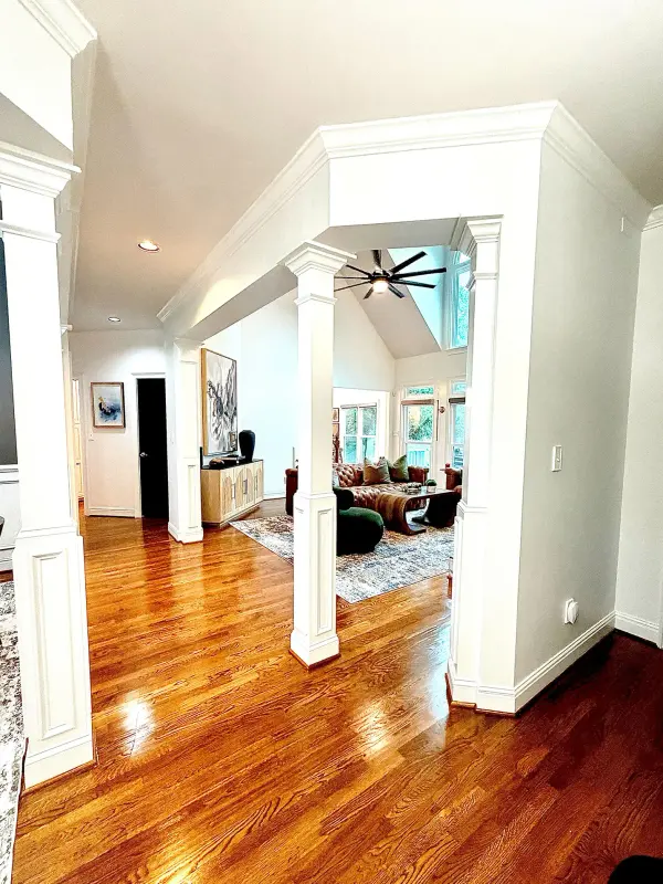Open living area with glossy oak floors, white walls and white square columns