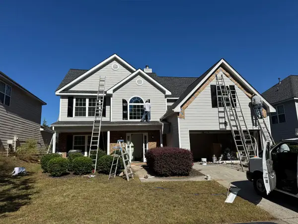 Two-story home with crews on ladders replacing siding on the garage gable