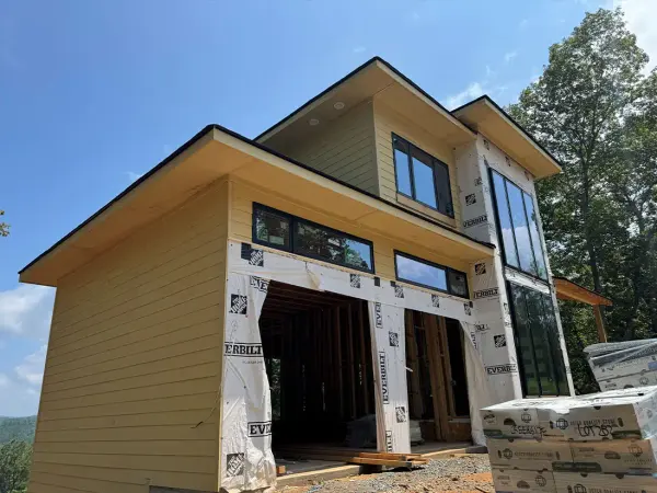 Modern new build with tan lap siding going up over house wrap around large window openings
