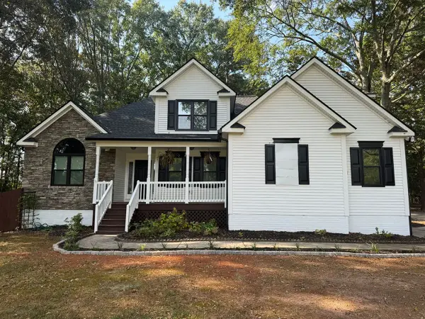 White sided farmhouse with a stone front, covered porch and black shutters