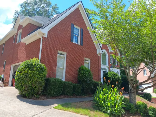 Side of a red brick home with white trim and black shutters behind shrubs