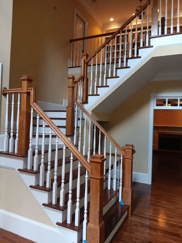 Two-story staircase with white balusters, stained oak handrails and newels, cream walls