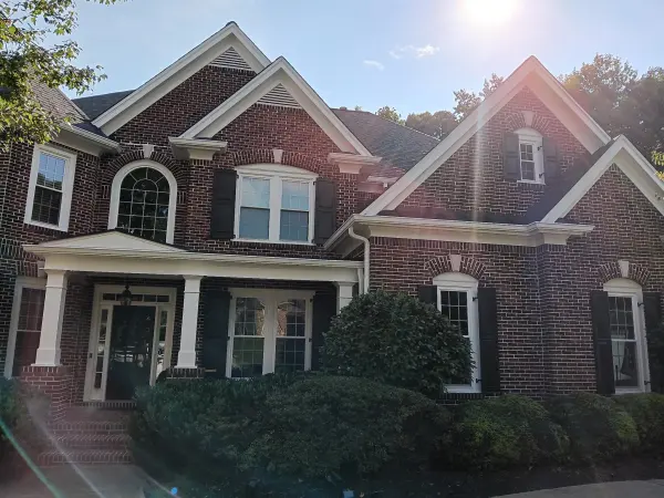 Red brick two-story home with white trim and black shutters, sun flare across the gable