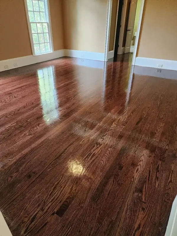 Red oak floor with a deep glossy finish reflecting the windows in an empty room