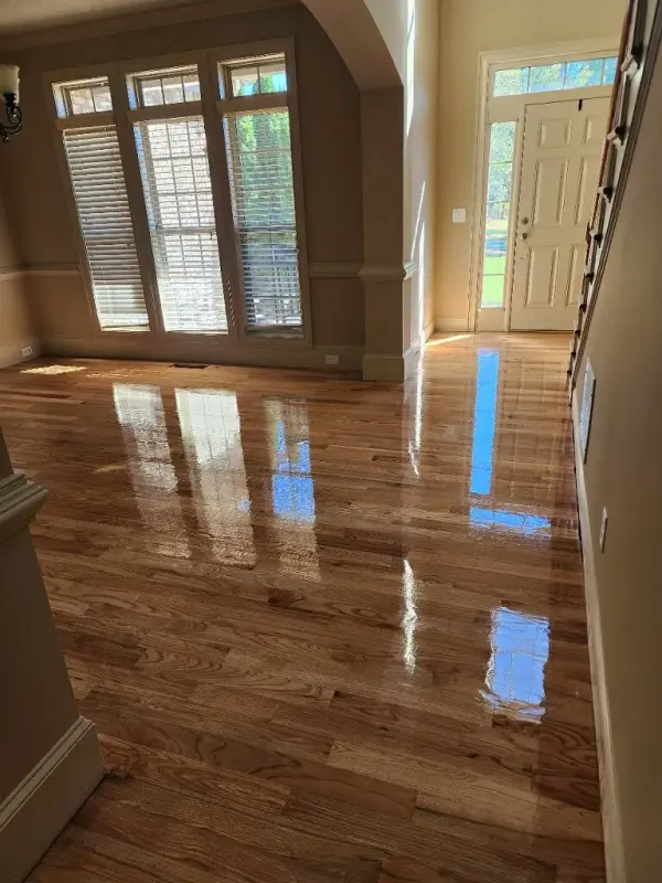 Glossy refinished hardwood in a two-story foyer with tall windows and a front door