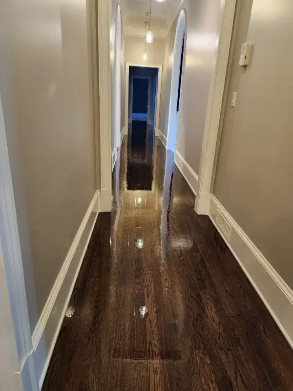 Long hallway with dark stained glossy hardwood and white baseboards