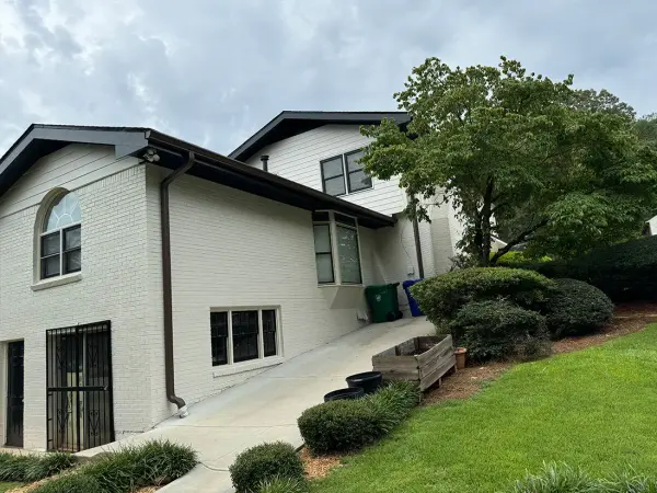 Side of a white painted brick home with dark brown gutters on a sloped yard