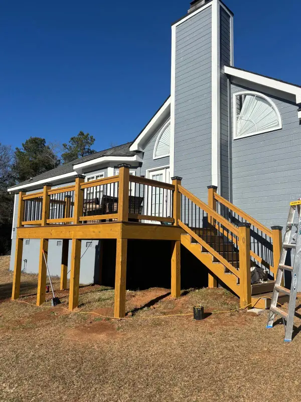 New pressure-treated deck with a stair and black balusters on the back of a gray home