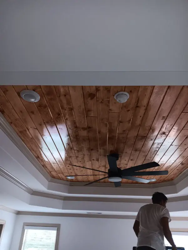 Stained cedar plank tray ceiling with a fan, a worker standing below