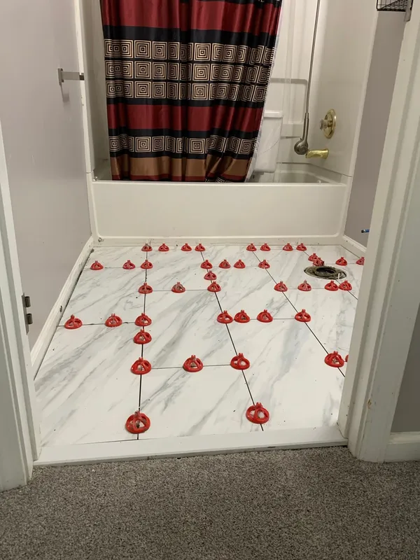 Marble-effect floor tile laid out with red leveling clips still in place