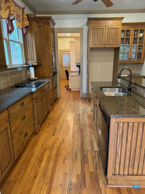 Galley kitchen with wood cabinets and granite tops over refinished oak flooring