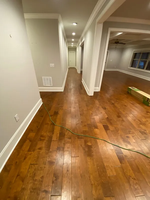 Refinished hardwood running the length of a hall into an open room, extension lead still out