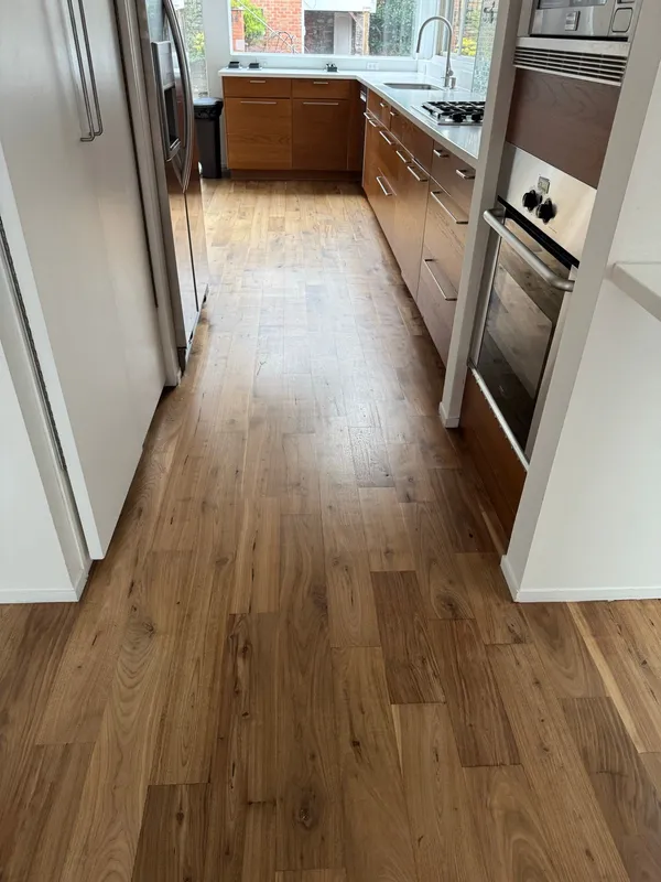 Galley kitchen with wood cabinets and a wall oven over wide plank wood flooring