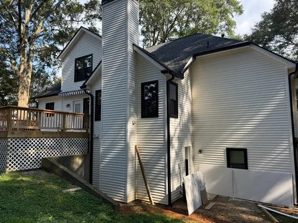 Rear of a home with new white vinyl siding on a tall chimney chase, spare panels leaning on the wall