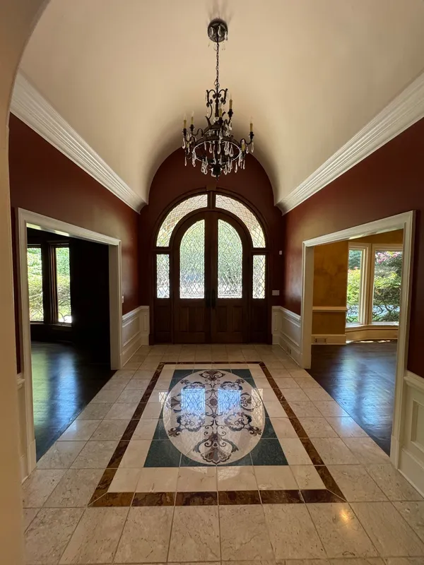Two-story entry with deep red walls, an arched door and a stone tile floor with an inlaid medallion